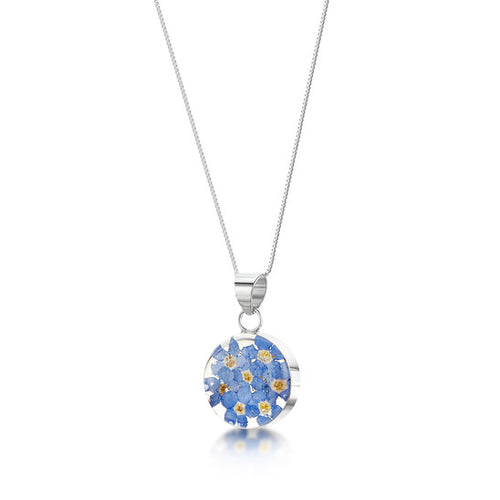The image shows a round sterling silver pendant. The pendant contains real forget-me-not flowers in a clear resin mounted within sterling silver on an 18 inch chain.